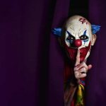 A clown from behind the scenes holds a finger to his mouth